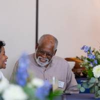 Gentleman sitting at table between two woman who are chatting together